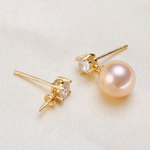 May include: A pair of gold earrings with a single pearl drop and a small clear cubic zirconia stone on each earring.
