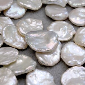 May include: A collection of white, irregular shaped, freshwater pearls. The pearls are smooth and have a slight iridescent sheen.