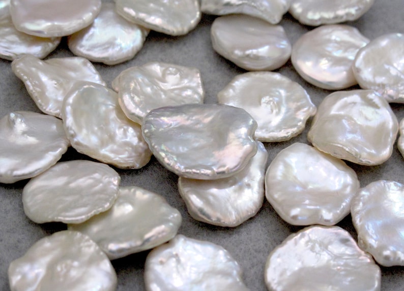 May include: A collection of white, irregular shaped, freshwater pearls. The pearls are smooth and have a slight iridescent sheen.