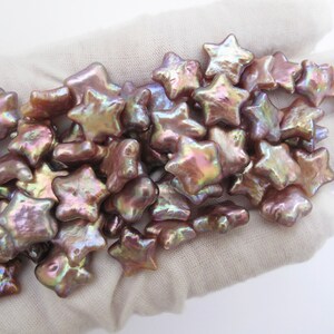 May include: A pile of iridescent pink and gold star-shaped pearl beads. The beads are arranged in a loose pile on a white surface.