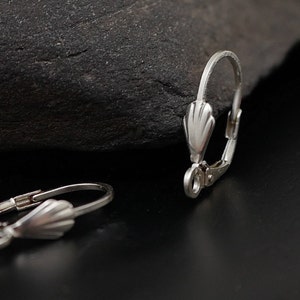 May include: Two silver earring hooks with a scalloped design. The hooks are made of metal and have a spring-loaded closure.