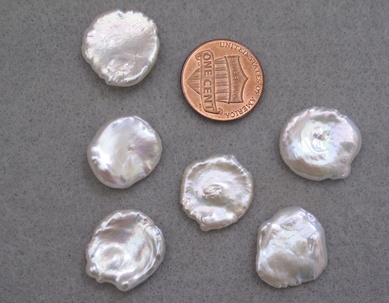 May include: Six white, round, irregular shaped, iridescent pearls, with one pearl slightly larger than the others, next to a US penny.