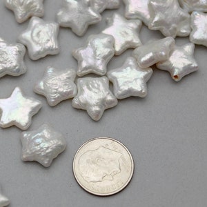May include: A collection of white pearl star-shaped beads. The beads are iridescent and have a slightly textured surface. The beads are scattered on a gray surface next to a US quarter.