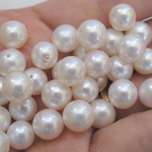May include: A collection of white pearl beads, some with iridescent highlights, arranged in a hand.