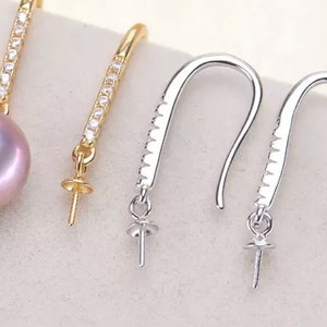Pode incluir: Tr&ecirc;s pares de fechos de brincos com uma configura&ccedil;&atilde;o para p&eacute;rola ou pedra preciosa. Os fechos s&atilde;o de metal prateado e dourado e t&ecirc;m um fecho de gancho. Os fechos est&atilde;o sobre uma superf&iacute;cie branca.