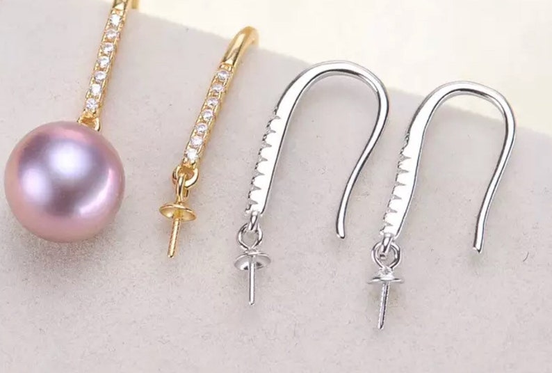Pode incluir: Tr&ecirc;s pares de fechos de brincos com uma configura&ccedil;&atilde;o para p&eacute;rola ou pedra preciosa. Os fechos s&atilde;o de metal prateado e dourado e t&ecirc;m um fecho de gancho. Os fechos est&atilde;o sobre uma superf&iacute;cie branca.