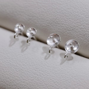 May include: Four small, silver-colored earring components are arranged in a row. Each component has a rounded, slightly textured top with a small loop extending from the bottom. The components are set against a light gray background.