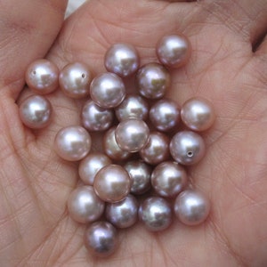 May include: A collection of round, iridescent pearls in shades of lavender and pink. The pearls are smooth and have a subtle sheen.