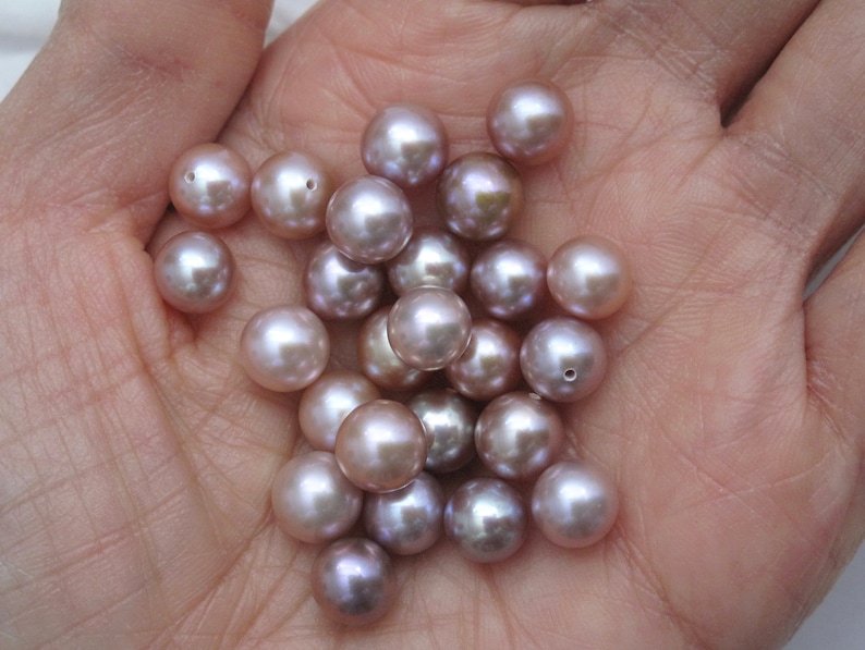 May include: A collection of round, iridescent pearls in shades of lavender and pink. The pearls are smooth and have a subtle sheen.