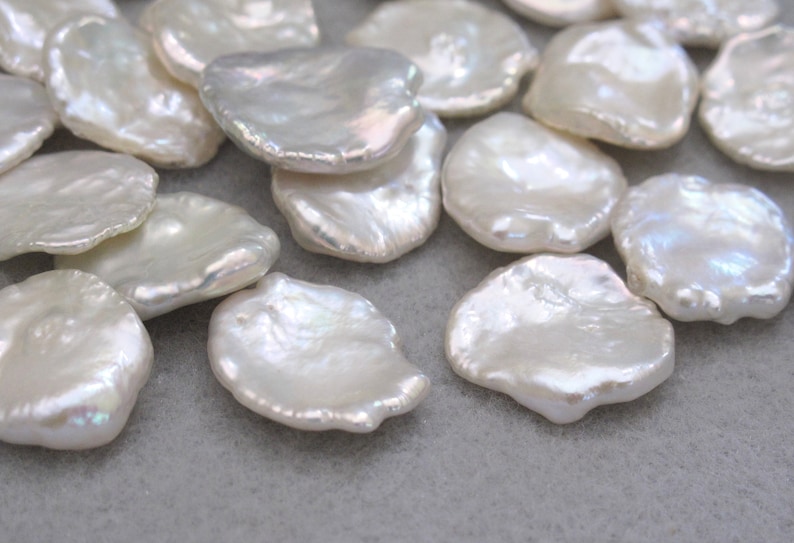 May include: A collection of white, irregularly shaped freshwater pearls. The pearls are smooth and have a slightly iridescent sheen.