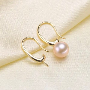 May include: A pair of gold-toned earrings with a single pearl dangling from each earring. The pearls are a light pink color.