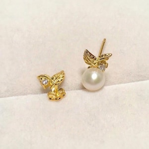 May include: A pair of gold earrings with a pearl and leaf design. One earring features a single pearl with a small diamond accent, while the other earring has a leaf design with a small diamond accent.