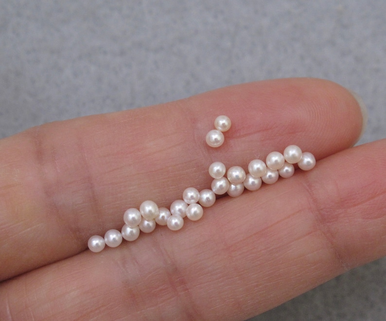 May include: A collection of small, white, round pearls, scattered on a hand.