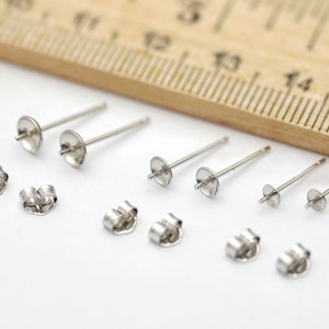May include: A set of six silver earring posts and backs. The posts are about 1.5 inches long and have a small round disc at the top. The backs are small and have a loop on the back.