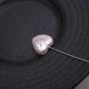 May include: A white heart-shaped pearl on a black plate with a silver pin attached.