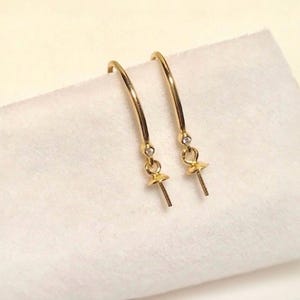 May include: A pair of gold-toned earring findings with a small clear rhinestone accent. The findings have a loop at the top and a small ball at the bottom with a hole for attaching a bead.