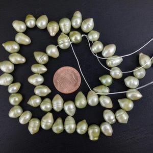 May include: A strand of light green baroque pearls, strung on white thread. The pearls are irregular in shape and have a slightly iridescent sheen.