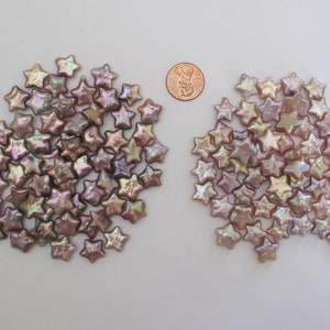 May include: Two piles of iridescent, light brown star-shaped pearl beads. The beads are about the size of a US penny.