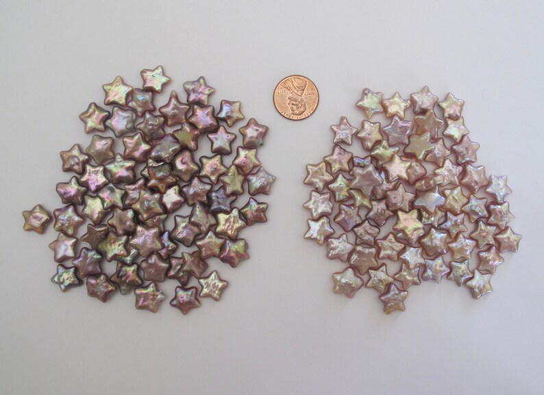 May include: Two piles of iridescent, light brown star-shaped pearl beads. The beads are about the size of a US penny.