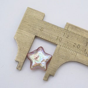 May include: A pink iridescent star-shaped pearl bead measured with a caliper. The bead is approximately 1.2 cm wide.