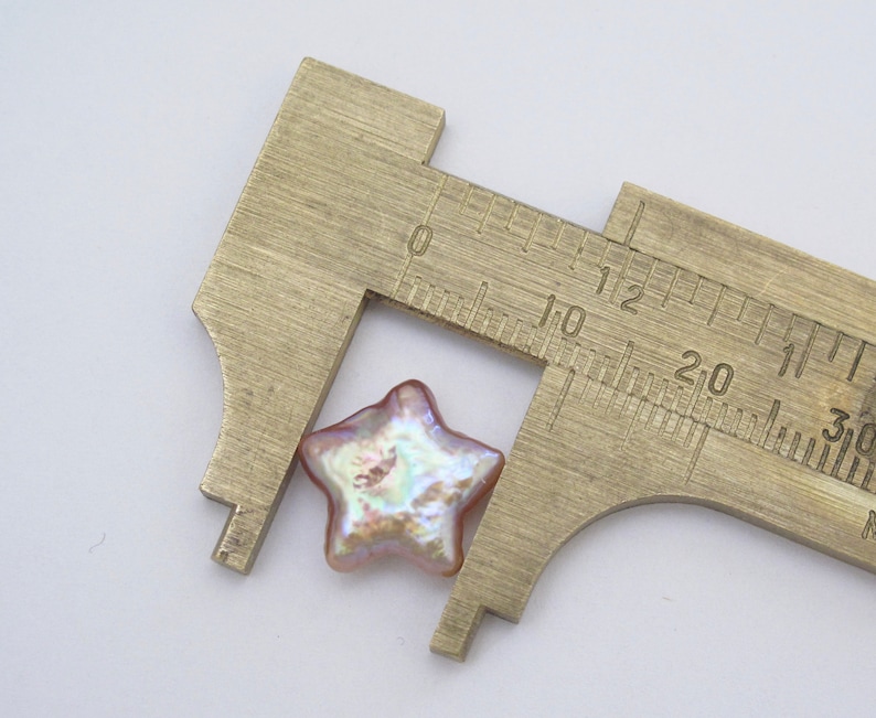 May include: A pink iridescent star-shaped pearl bead measured with a caliper. The bead is approximately 1.2 cm wide.