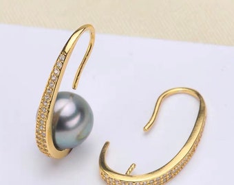 May include: A pair of gold earrings with a black pearl and a row of small clear stones. The earrings are designed with a curved shape and a hook closure.