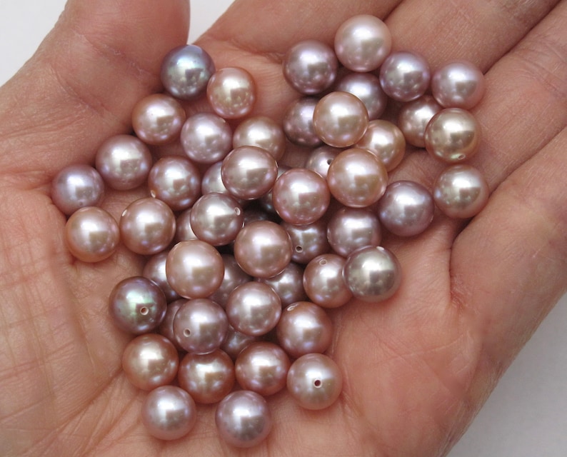 May include: A collection of round, iridescent pearls in shades of lavender, pink, and white. The pearls are smooth and have a subtle sheen.