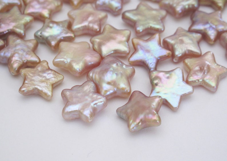 May include: A collection of iridescent pink star-shaped pearl beads. The beads are smooth and have a pearlescent finish.
