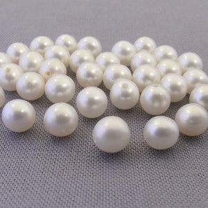 May include: A collection of white pearl beads, arranged in a loose pile on a gray surface.