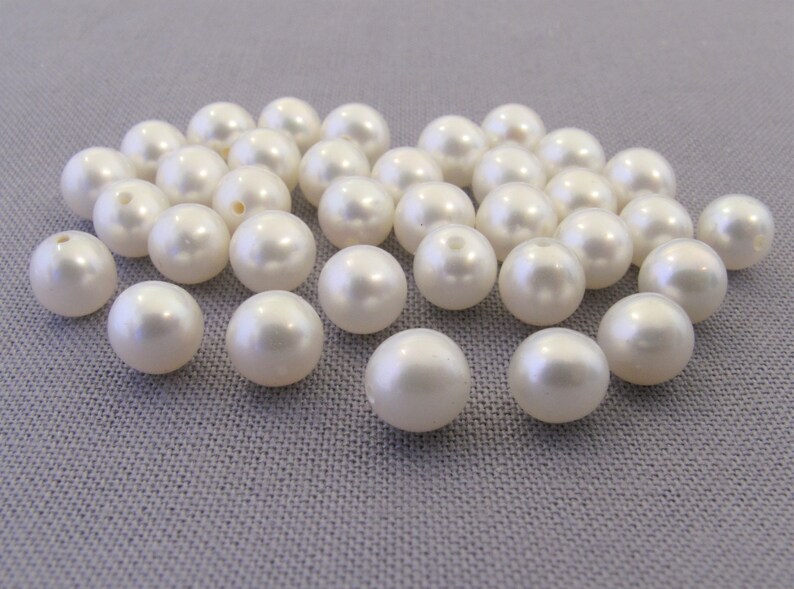 May include: A collection of white pearl beads, arranged in a loose pile on a gray surface.