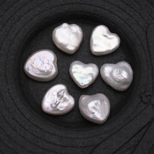 May include: Seven white heart-shaped pearl beads on a black background.