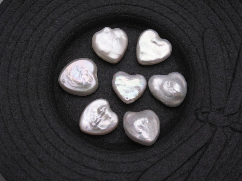May include: Seven white heart-shaped pearl beads on a black background.