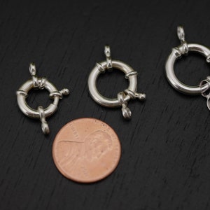 Puede incluir: Tres cierres de metal plateados para la elaboración de joyas. Los cierres son redondos con un diseño de nudo decorativo y una pequeña bola en el lateral. Los cierres son aproximadamente del tamaño de una moneda de un céntimo de euro.