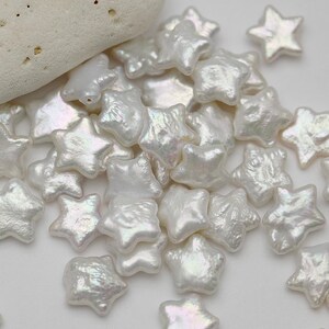 May include: A pile of white pearl star-shaped beads. The beads have an iridescent sheen.