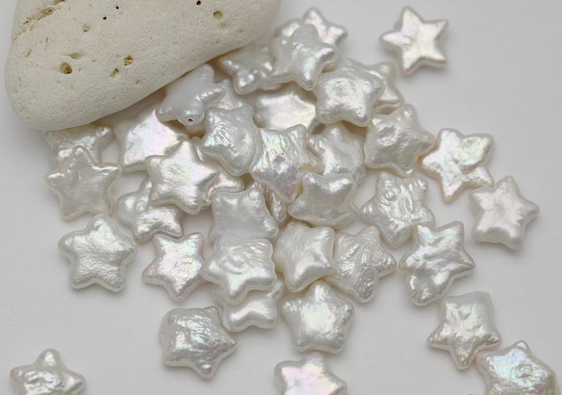 May include: A pile of white pearl star-shaped beads. The beads have an iridescent sheen.