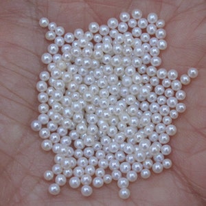 May include: A large pile of white round pearls, scattered on a hand.
