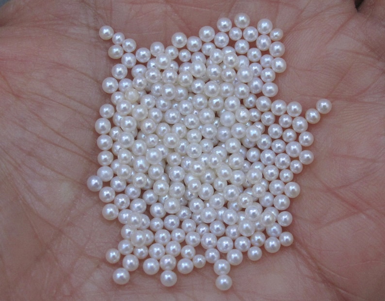 May include: A large pile of white round pearls, scattered on a hand.