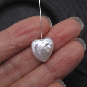 May include: A white heart-shaped pearl with an iridescent sheen, suspended from a silver wire.