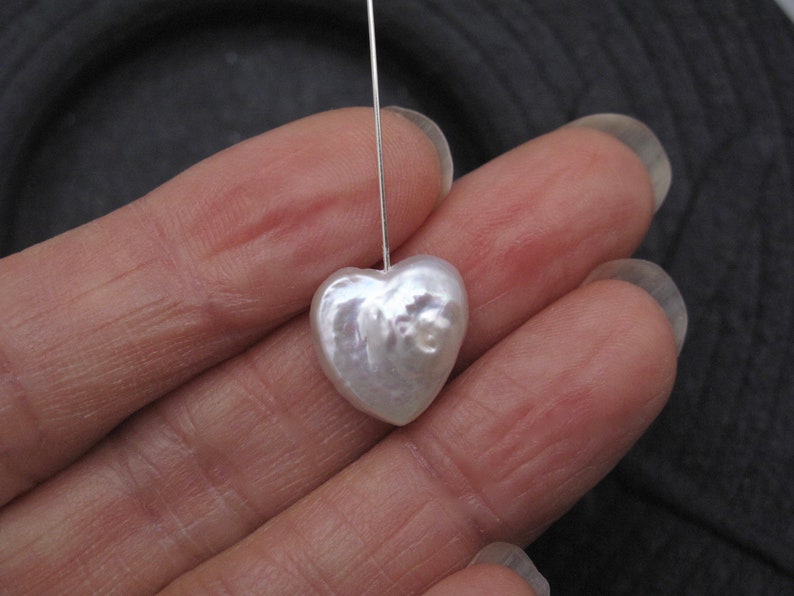 May include: A white heart-shaped pearl with an iridescent sheen, suspended from a silver wire.