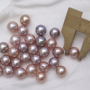 May include: A group of 20 light purple and lavender pearls with a ruler measuring one of the pearls at 10 mm. The pearls are round and have a smooth, glossy finish.