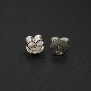 May include: A pair of silver earring backs with a push-back closure. The back of one earring back has the marking "S925" on it.