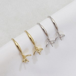 May include: Two pairs of earring settings, one gold and one silver, with a round bezel for a pearl or gemstone. The settings are on a white surface.
