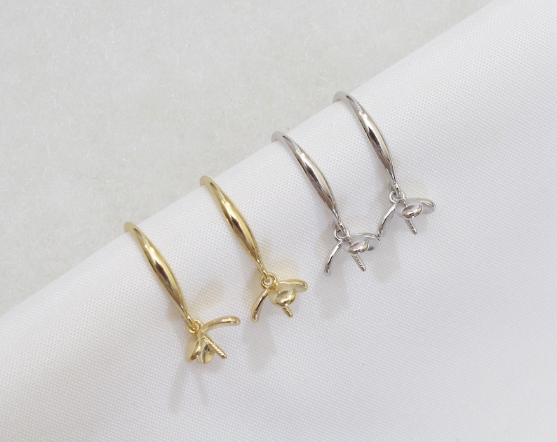 May include: Two pairs of earring settings, one gold and one silver, with a round bezel for a pearl or gemstone. The settings are on a white surface.