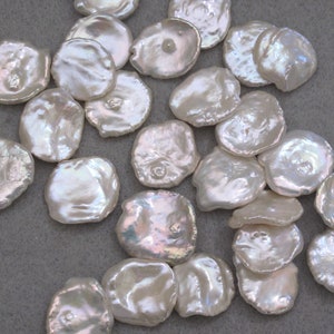 May include: A collection of white, round, flat, iridescent, mother-of-pearl shell beads. The beads are smooth and have a slightly irregular shape.
