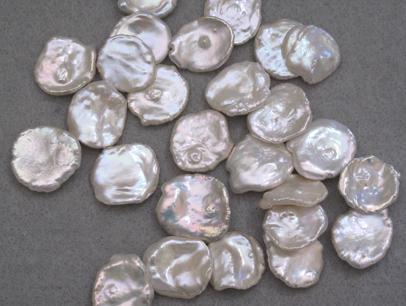 May include: A collection of white, round, flat, iridescent, mother-of-pearl shell beads. The beads are smooth and have a slightly irregular shape.