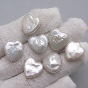May include: Seven white heart-shaped pearls on a white fabric background.