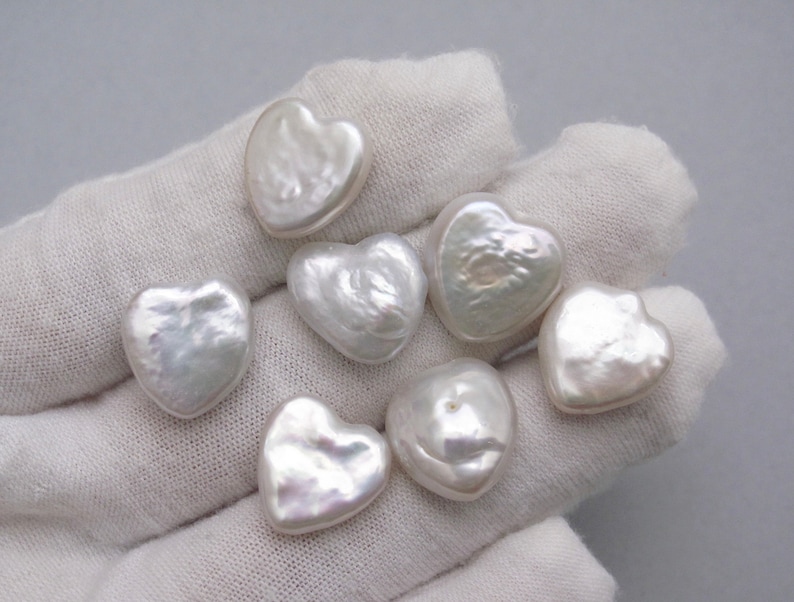 May include: Seven white heart-shaped pearls on a white fabric background.