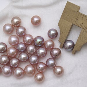 May include: A collection of 20 iridescent purple pearls, some of which are being measured with a ruler. The pearls are approximately 10mm in diameter.