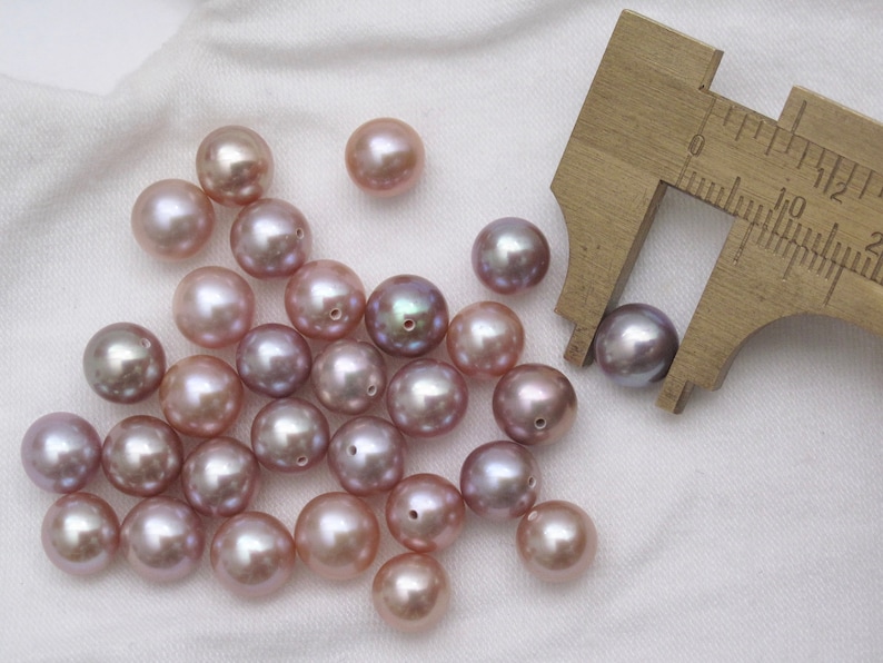 May include: A collection of 20 iridescent purple pearls, some of which are being measured with a ruler. The pearls are approximately 10mm in diameter.