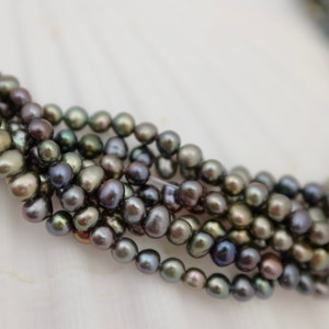 Può includere: Una collana di perle d'acqua dolce di colore verde scuro e nero. Le perle sono rotonde e hanno una leggera lucentezza iridescente.